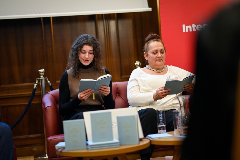 Zwei Frauen sitzen im Lesesaal und lesen in Büchern. Ein Tisch mit mehreren Buchköpfen ist sichtbar.