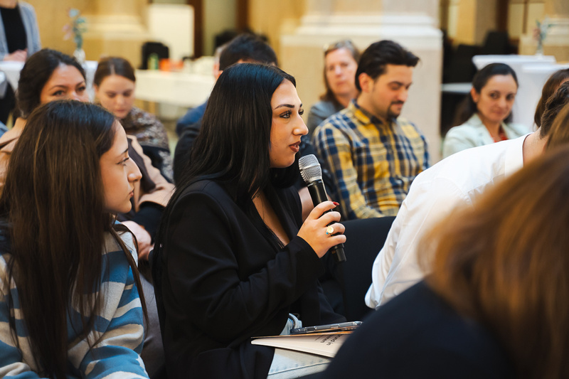 Frau spricht mit Mikrofon in einer Zuschauergruppe.