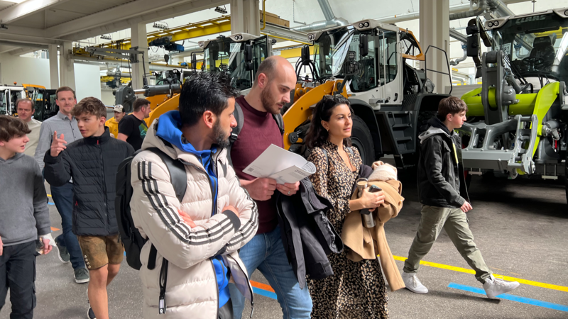 Eine Gruppe von Menschen besichtigt Traktoren in einer Lagerhalle.