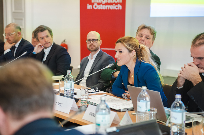 Eine Diskussion in einem Konferenzraum mit mehreren Teilnehmern, wo eine Frau mit Mikrofon spricht.