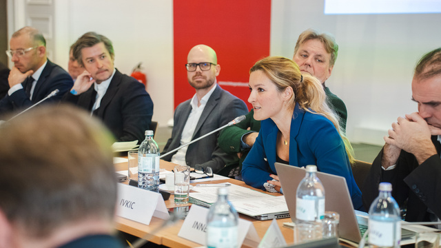 Eine Diskussion in einem Konferenzraum mit mehreren Teilnehmern, wo eine Frau mit Mikrofon spricht.