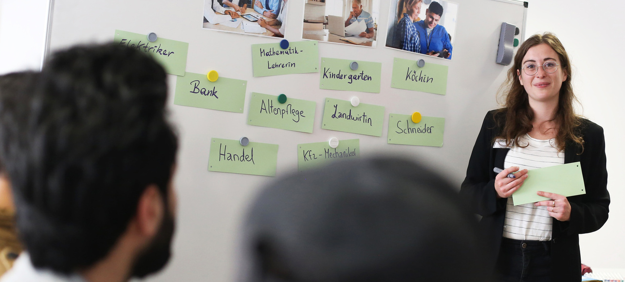 Eine Frau präsentiert an einem Whiteboard mit Berufen und Bildern von Menschen in verschiedenen Arbeitsumgebungen.