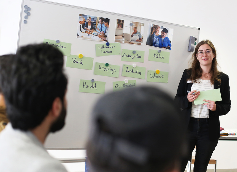 Eine Frau präsentiert an einem Whiteboard mit Berufen und Bildern von Menschen in verschiedenen Arbeitsumgebungen.