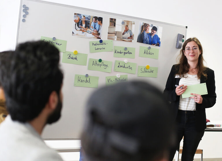 Eine Frau präsentiert an einem Whiteboard mit Berufen und Bildern von Menschen in verschiedenen Arbeitsumgebungen.