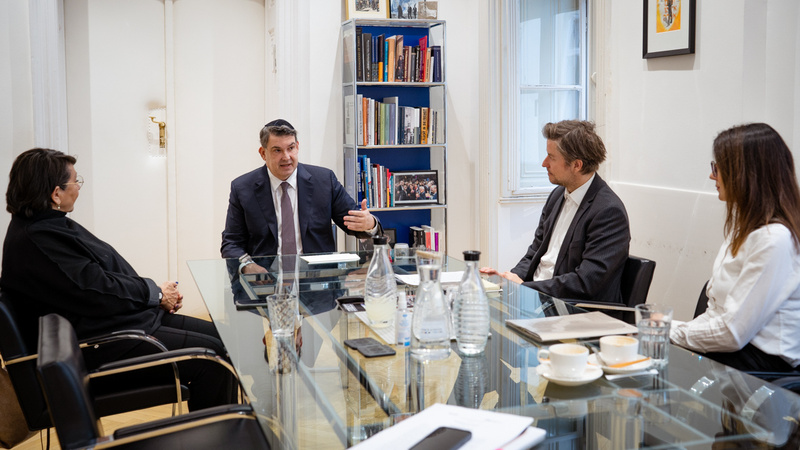 Vier Personen sitzen an einem Glastisch und diskutieren in einem hellen Raum.