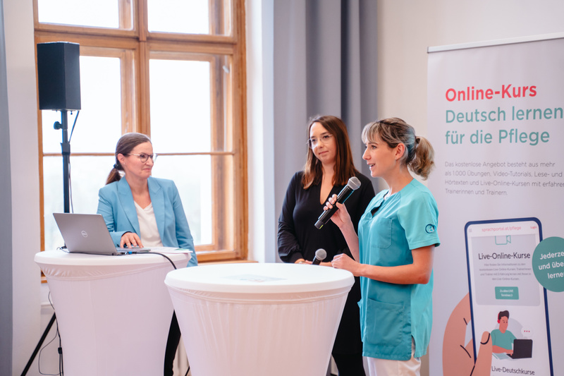Drei Frauen präsentieren einen Online-Deutschkurs für Pflegekräfte im Rahmen einer Veranstaltung.