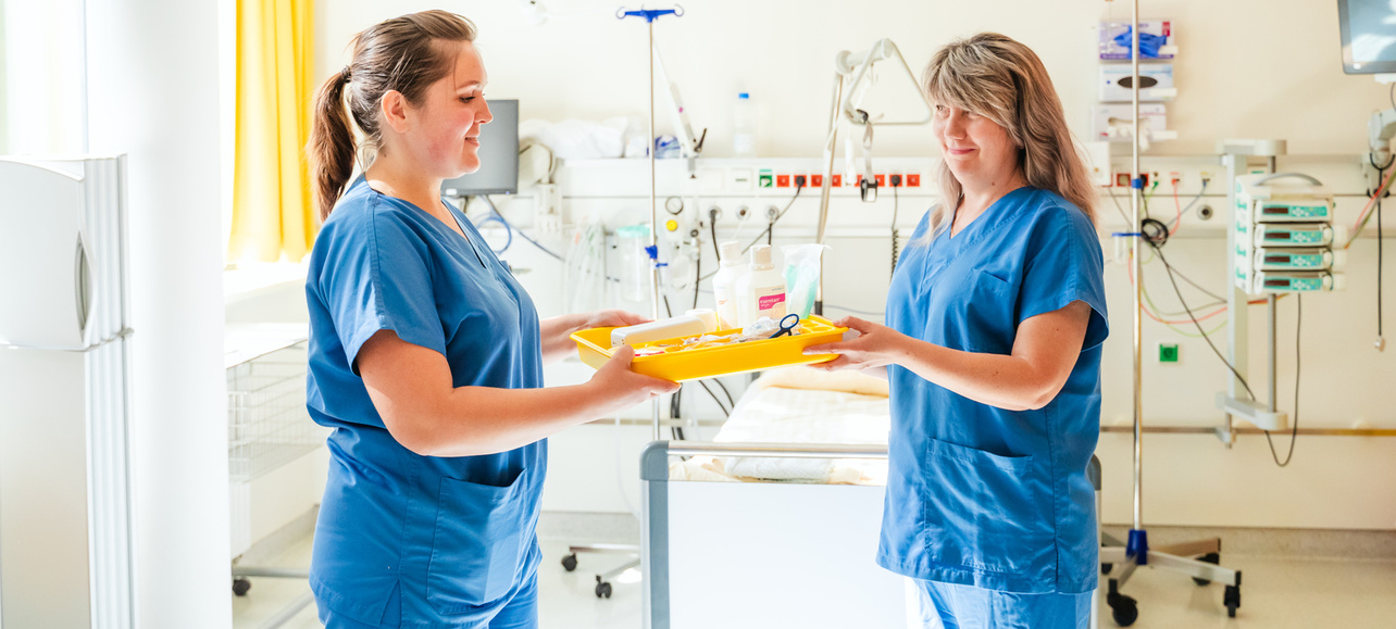 Zwei Krankenschwestern übergeben sich ein Tablett.