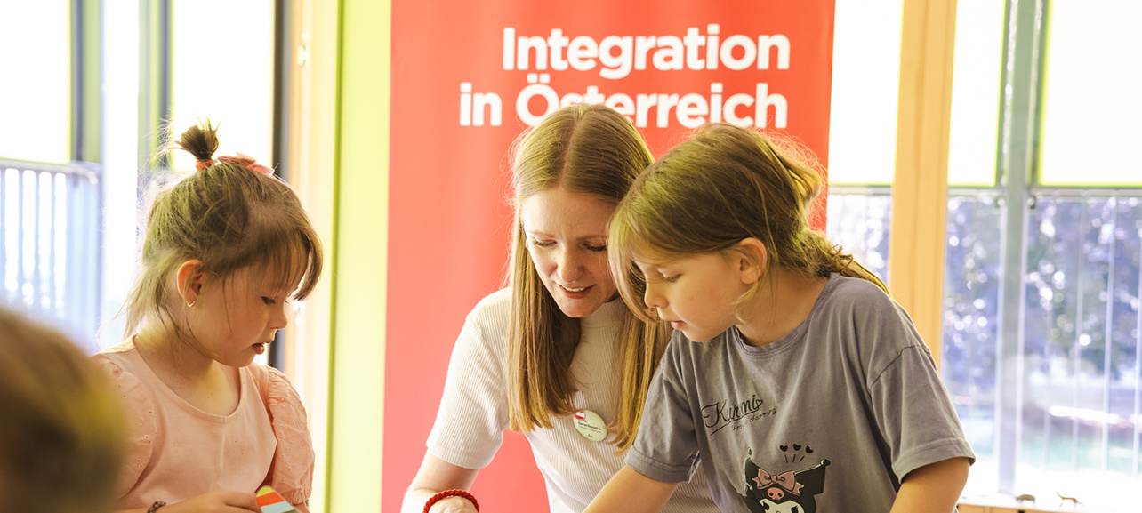 Eine Frau arbeitet mit zwei Kindern an einem Tisch, um Integration in Österreich zu fördern.