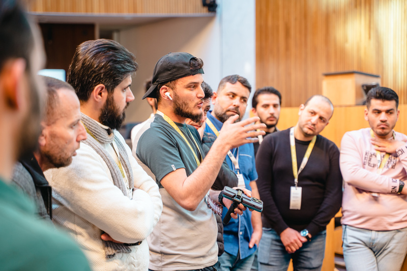 Eine Gruppe von Männern hört aufmerksam einem Redner zu, der mit einer Fernbedienung präsentiert.