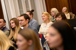 Eine Gruppe von Menschen sitzt aufmerksam und hört zu, einige lächeln während einer Veranstaltung.