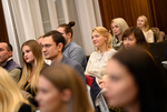 Eine Gruppe von Menschen sitzt aufmerksam und hört zu, einige lächeln während einer Veranstaltung.