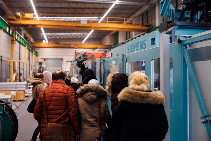 Eine Gruppe von Menschen steht in einer Fabrikhalle an Maschinen entlang.