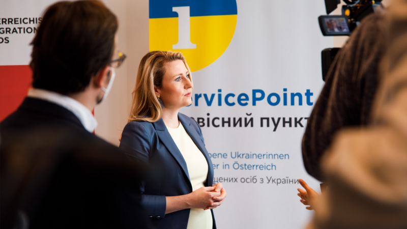 Eine Person steht vor einem Plakat mit der Aufschrift "ServicePoint" und spricht mit einem Journalisten.