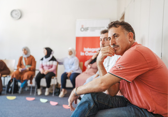 Eine Gruppe von Menschen sitzt in einem Raum, während ein Mann nachdenklich zu hören scheint.