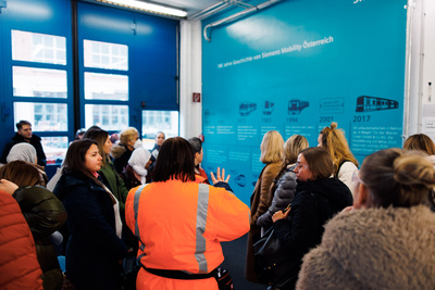 Gruppe von Menschen während einer Präsentation vor einer Wand mit Informationen über Siemens Mobility Österreich.
