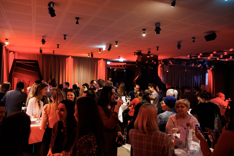 Belebte Veranstaltung mit fröhlichen Menschen, die miteinander sprechen und Getränke genießen, in sanftem rotem Licht.