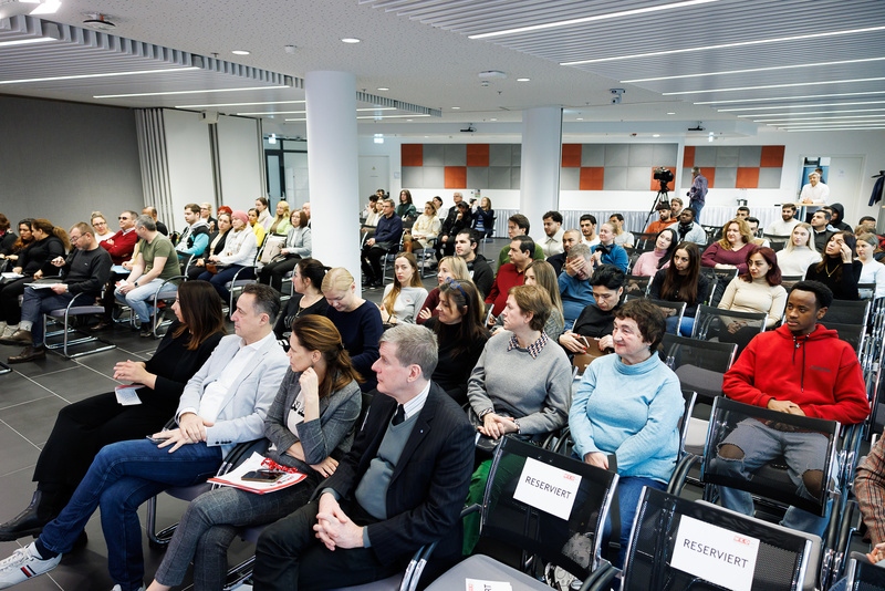 Eine große Gruppe von Menschen sitzt in einem modernen Raum und hört einer Präsentation zu.