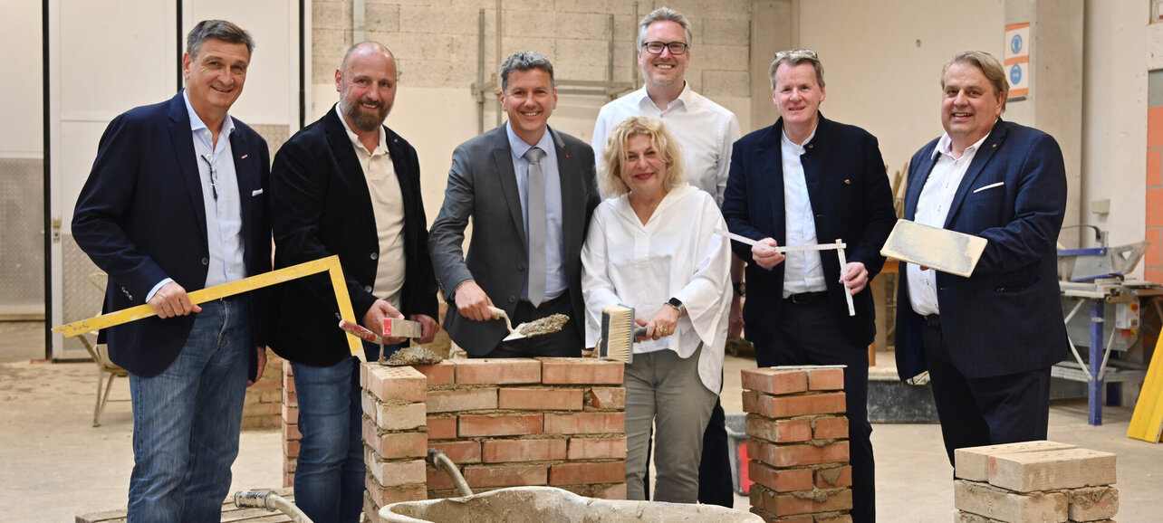 Sechs Personen mit Handwerkzeugen und Bausteinen beim gemeinsamen Foto