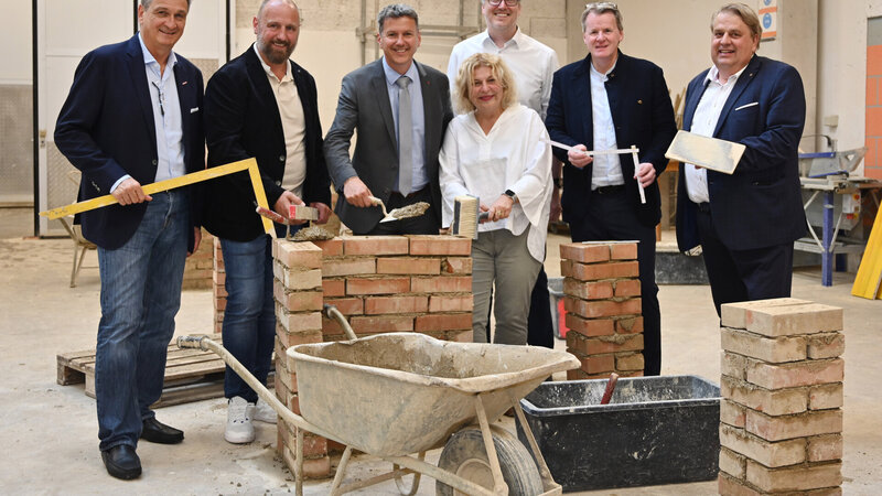 Sechs Personen mit Handwerkzeugen und Bausteinen beim gemeinsamen Foto