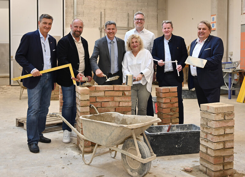 Sechs Personen mit Handwerkzeugen und Bausteinen beim gemeinsamen Foto