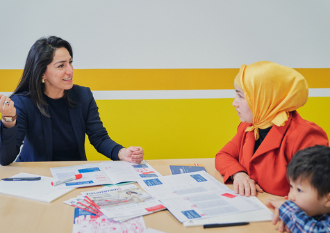 Zwei Frauen und ein Junge sitzen am Tisch und diskutieren über Unterlagen und Informationsmaterialien.