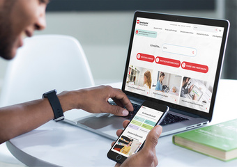 Person nutzt ein Smartphone und Laptop, um auf eine Website zuzugreifen.