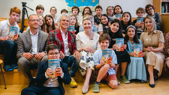 Eine Gruppe von Kindern und Erwachsenen hält Bücher in die Kamera und lächelt zusammen.