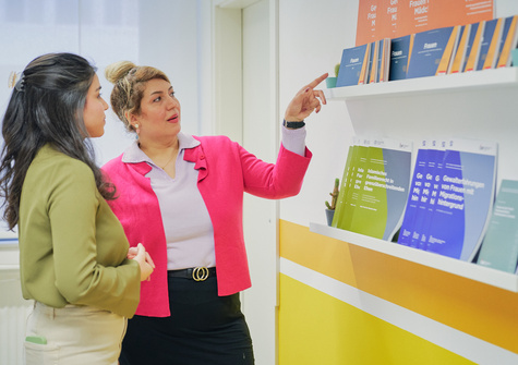 Zwei Frauen betrachten Informationen über Frauenrechte, während eine auf ein Plakat zeigt.