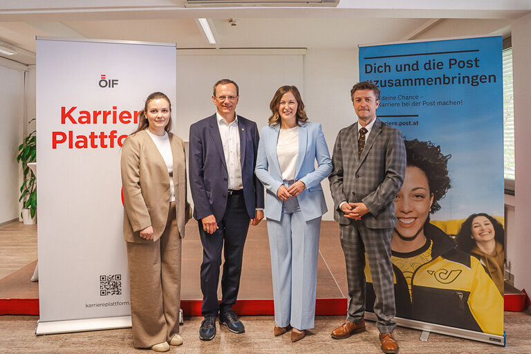 Eine Gruppe von vier Personen steht vor zwei Bannern in einem Raum. Links ist ein Banner mit der Aufschrift „Karrieren Plattform“. Rechts steht ein Banner mit dem Text „Dich und die Post zusammenbringen“. Alle Personen tragen formelle Kleidung und lächeln in die Kamera.
