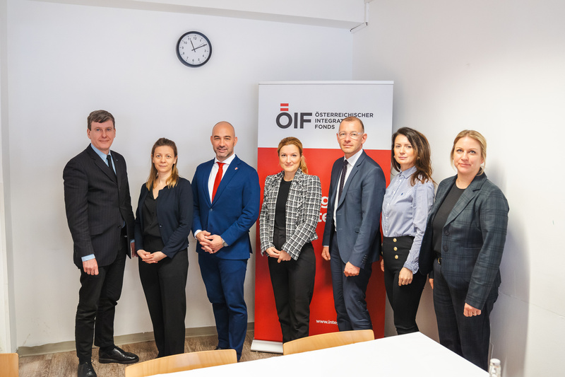 Eine Gruppe von sechs Personen steht zusammen vor einem Banner des Österreichischen Integrationsfonds in einem Büro.