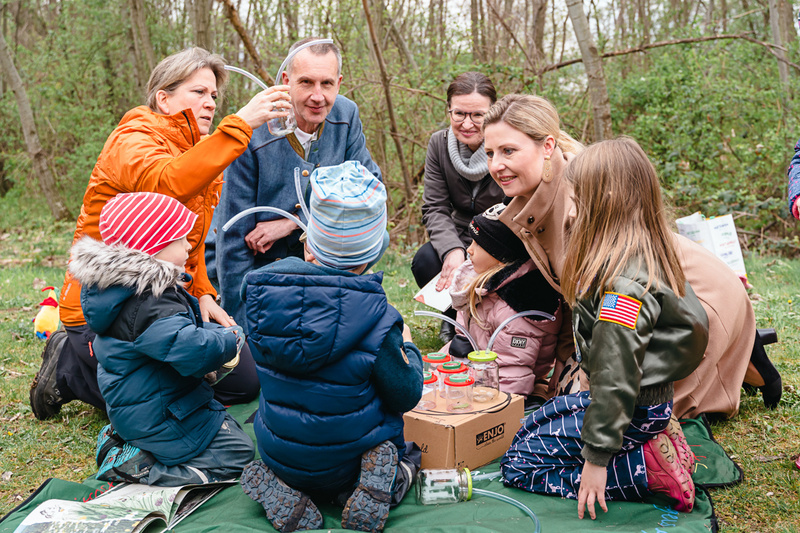 Eine Gruppe von Erwachsenen und Kindern experimentiert gemeinsam im Freien mit Flaschen und Schläuchen.