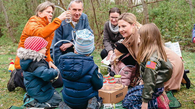 Eine Gruppe von Erwachsenen und Kindern experimentiert gemeinsam im Freien mit Flaschen und Schläuchen.
