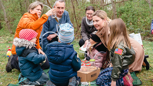 Eine Gruppe von Erwachsenen und Kindern experimentiert gemeinsam im Freien mit Flaschen und Schläuchen.