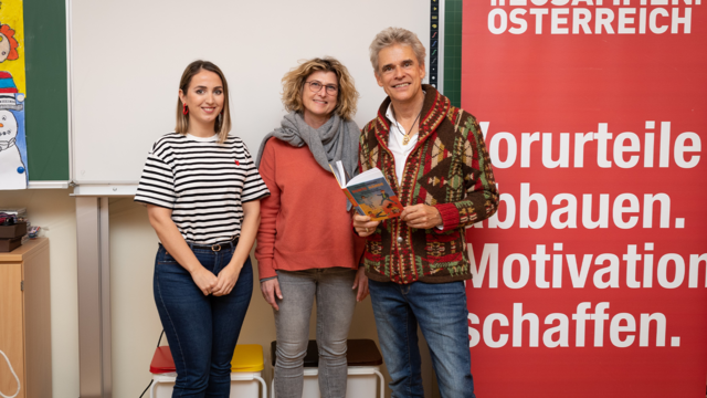 Drei Personen stehen vor einer Wand mit einem roten Banner über Vorurteile und Motivation.