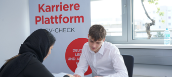 Zwei Personen bei einem Beratungsgespräch, im Hintergrund ein Banner mit Informationen zur Karriereplattform.