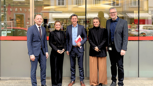 Fünf Personen stehen vor einem Gebäude und lächeln in die Kamera.