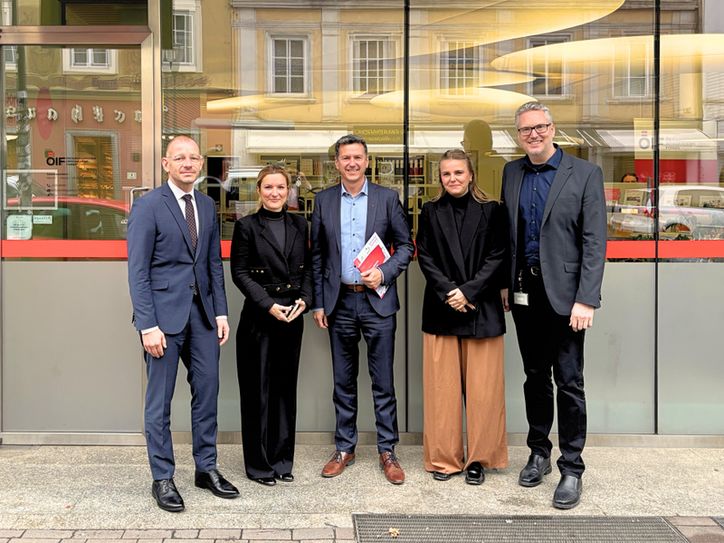 Fünf Personen stehen vor einem Gebäude und lächeln in die Kamera.