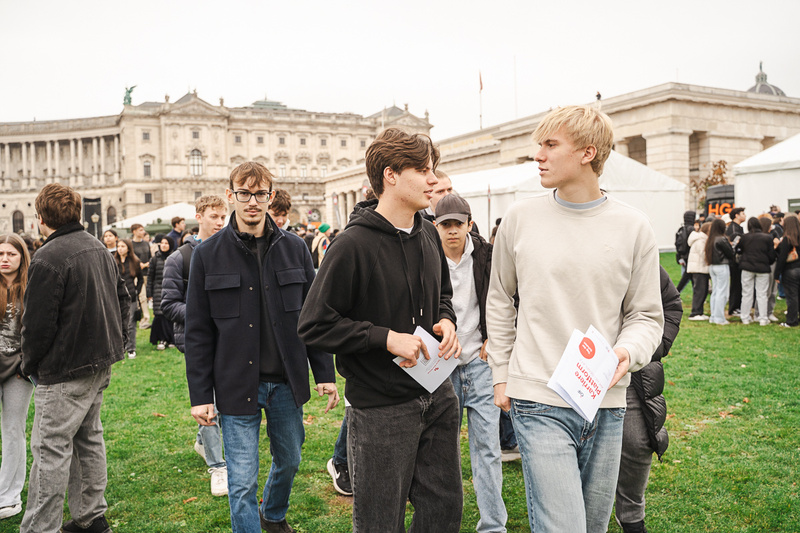 Junge Menschen stehen auf einer Wiese und unterhalten sich, während sie Informationsmaterial in den Händen halten.