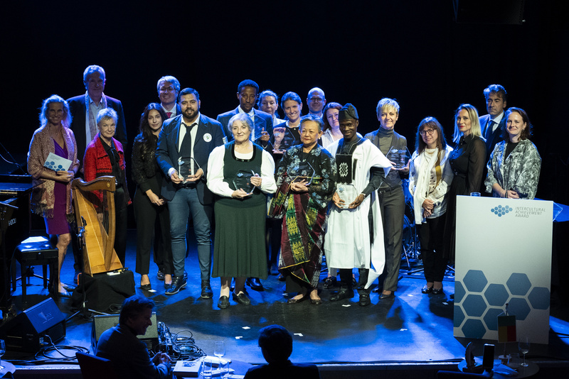 Eine Gruppe von Menschen hält Auszeichnungen bei einer interkulturellen Preisverleihung auf einer Bühne.