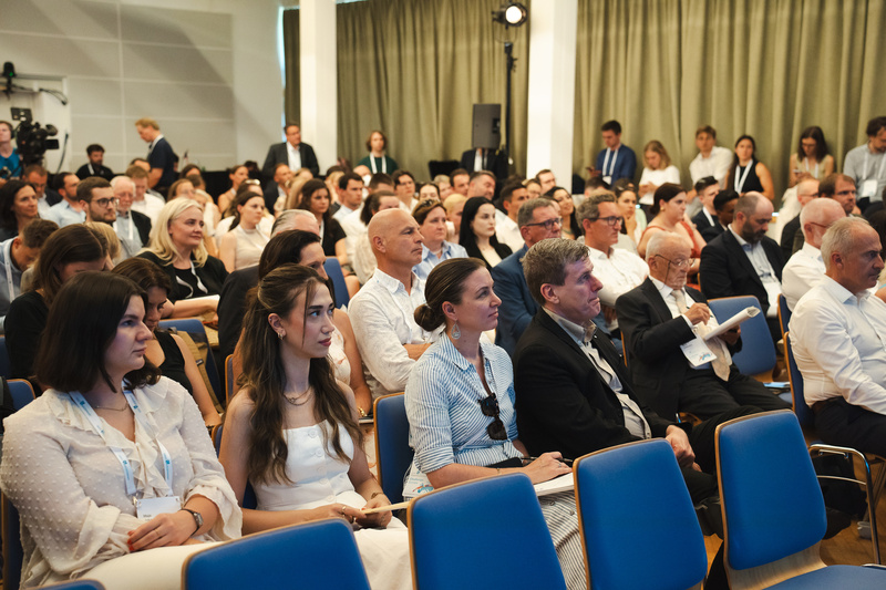 Eine große Gruppe von Menschen sitzt aufmerksam in einem Konferenzraum während einer Veranstaltung.
