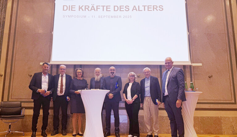 Eine Gruppe von acht Menschen steht vor einem Banner, das 