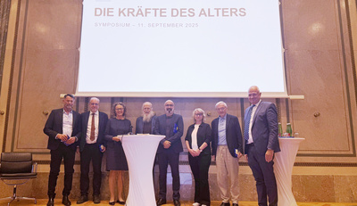 Eine Gruppe von acht Menschen steht vor einem Banner, das "Die Kräfte des Alters" anzeigt.