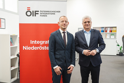 Zwei Männer stehen vor einem Banner des Österreichischen Integrationsfonds in einem modernen Büro.