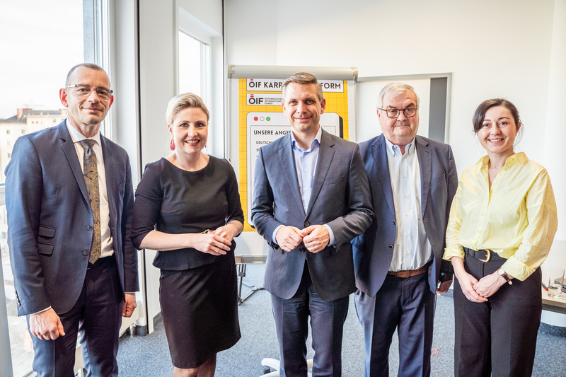 Fünf Personen stehen in einem Raum zusammen, lächeln und posieren für ein Foto.