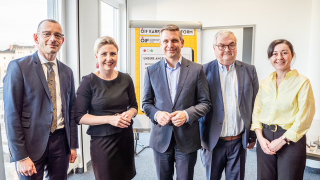 Fünf Personen stehen in einem Raum zusammen, lächeln und posieren für ein Foto.