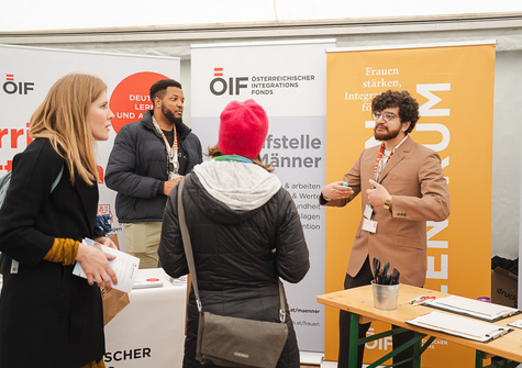 Zwei Männer und eine Frau sprechen an einem Informationsstand zum Thema Integration und Frauenförderung.