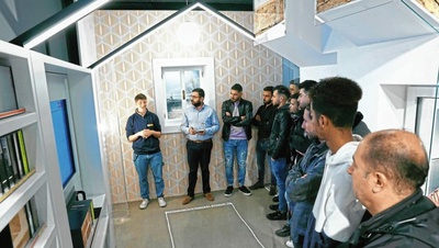 Eine Gruppe von Menschen hört einem Vortrag in einem modernen, hausähnlichen Raum zu.