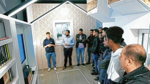Eine Gruppe von Menschen hört einem Vortrag in einem modernen, hausähnlichen Raum zu.