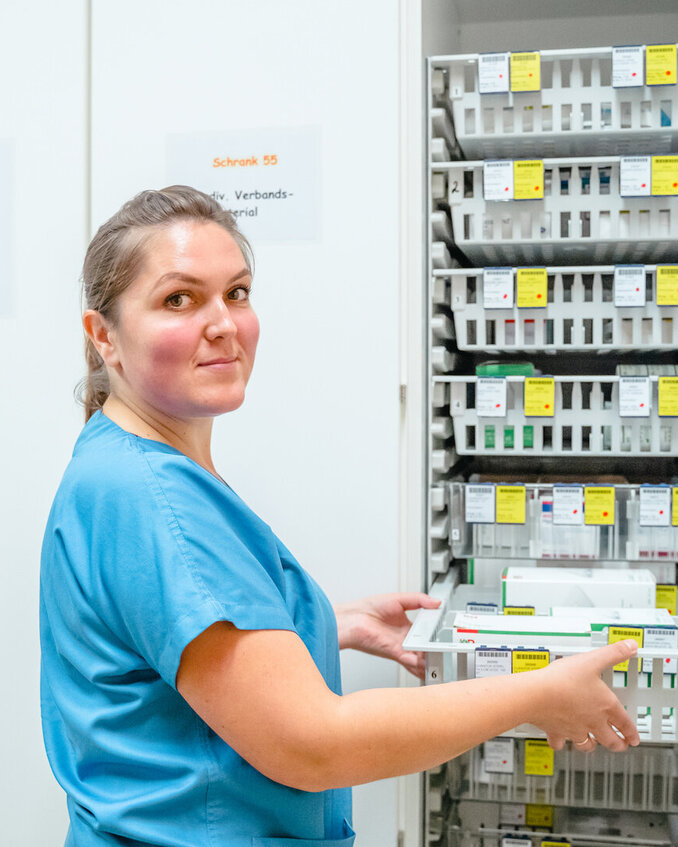 Eine Pflegekraft entnimmt ein Fach mit Materialien aus einem Krankenhausregal.