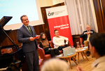 Veranstaltung über Integration in Kärnten mit mehreren Rednern und einem Klavier im Hintergrund.